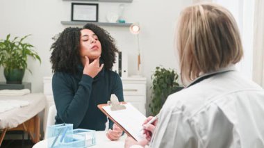 Muhtelif bir kadın sağlık semptomlarını tıbbi danışmanlık sırasında profesyonel bir doktora anlatır. Bu etkileşim, klinik bir ortamda hasta-doktor iletişimini, bakımını ve sağlık bilincini vurgular.