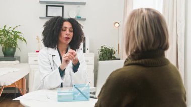 Beyaz önlüklü farklı bir kadın doktor, önemli sağlık bilgilerini tartışmak için hastasıyla ilgilenir ve profesyonel bir konsültasyon yapar. Bu tıbbi etkileşim modern bir klinik ortamında güven ve açık iletişimi vurgular..