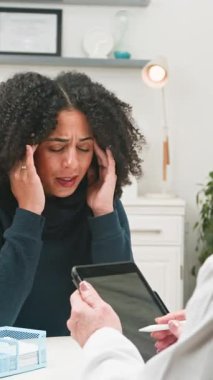 A female patient suffering from a severe headache or migraine is seen consulting with her doctor. The doctor reviews symptoms on a tablet, providing medical advice and care for health issues.