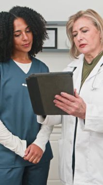 Two medical professionals, an experienced doctor and a younger nurse, are intently discussing patient information while looking at a digital tablet. They demonstrate teamwork and modern healthcare practices in a clinic.