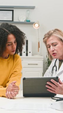 A female doctor and patient engage in a medical consultation. The physician provides healthcare information using a digital tablet, demonstrating modern diagnostic and treatment methods for patient health.