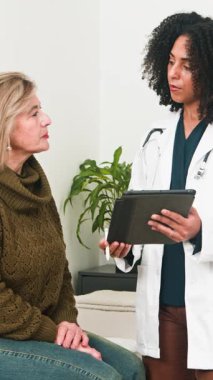 A skilled doctor uses a digital tablet to explain important medical information to a mature female patient. This professional consultation highlights modern healthcare communication and patient care in a clinic setting.