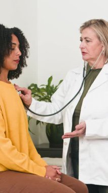 A caring doctor performs a thorough medical checkup on a young female patient using a stethoscope. This scene depicts professional healthcare services and patient-doctor interaction in a modern clinic setting.