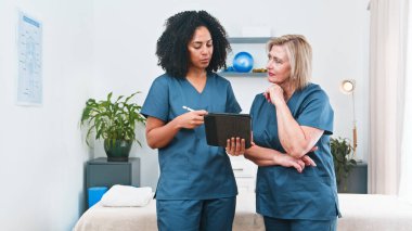 Two healthcare professionals in blue scrubs review a treatment plan on a tablet with a senior woman, highlighting collaboration, care, and patient-focused physiotherapy in a clinical setting.
