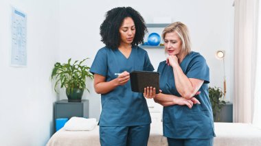 Two healthcare professionals in blue scrubs review a treatment plan on a tablet in a clinical setting, illustrating collaboration, patient care, and personalized physiotherapy guidance.