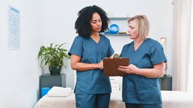 Two healthcare professionals in blue scrubs review a treatment plan on a clipboard in a calm clinic setting. They discuss exercises, rehabilitation, and patient care, highlighting teamwork and compassionate physiotherapy.
