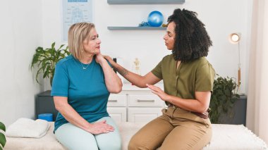 A friendly physiotherapist guides a senior woman through arm and shoulder exercises in a calm clinic room, emphasizing care, mobility improvement, and personalized rehabilitation.