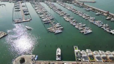Hava aracı, güneşli bir günde limana yanaşmış sayısız yat, yelkenli ve motorlu tekne ile dolu modern bir marinanın üzerinde yavaşça uçuyor.