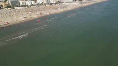 Güneşli bir günde birçok insanın yüzdüğü ve şemsiyelerin altında dinlendiği kalabalık kumlu bir plaj. Yaz tatilindeki tatil beldesinin havadan çekimi.
