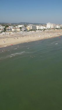 Güneşli bir yaz gününde popüler bir turist sahil beldesinin manzaralı manzarası. Denizde yüzen ve kalabalık kıyılarda dinlenen insanlar.