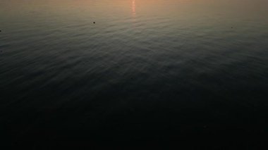 Güneşin ufukta yükseldiği sakin bir okyanusun havadan görünüşü. Durgun su, sabah gökyüzünün ılık renklerini yansıtır.