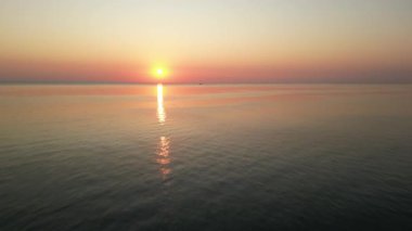 Görkemli gündoğumu sıcak renklerle gökyüzünü boyuyor. Sakin okyanus yüzeyi güneş ışığını mükemmel bir şekilde yansıtır. Huzurlu ve huzurlu bir deniz manzarası yaratır.