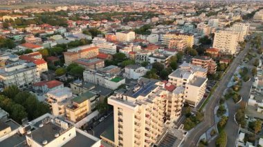 Geniş hava manzarası günbatımının sıcak ışığıyla aydınlanan otelleri, daireleri ve caddeleri olan modern bir kıyı şehrini yavaş yavaş gözler önüne seriyor.
