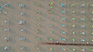 Üst aşağı hava manzarası kumlu deniz kıyısında boş güneş pansiyonları ve kapalı plaj şemsiyelerini gösteriyor. Sezon dışı veya salgın hastalık seyahati kavramı