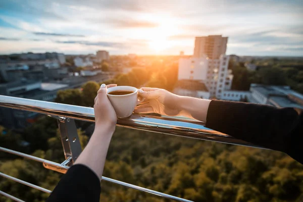 La mano femminile tiene la tazza con caffè o tè in raggi di tramonto ; — Foto Stock
