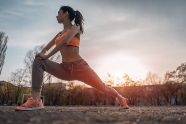 Çekici esmer kadın ısınıyor ve gün ışığında parkta esniyor.