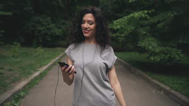 Bonita morena hembra sonriendo y escuchando música de jugador en parque — Vídeos de Stock