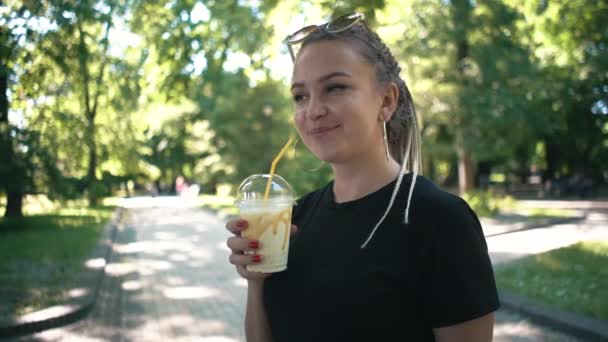 Mladá krásná dušička konzumní mléčný koktejl s karamelem ve slunném parku — Stock video