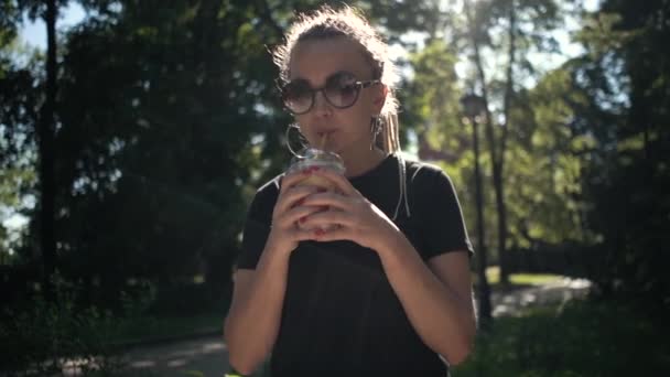 Junge schöne geflochtene Frau trinkt Milchshake mit Karamell im sonnigen Park — Stockvideo