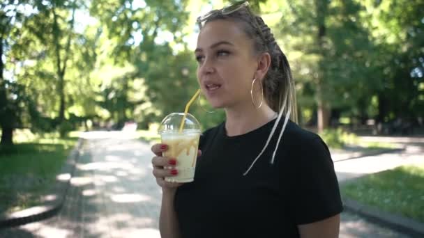 Fiatal gyönyörű fonott női ivás turmix karamell a napfényes parkban — Stock videók