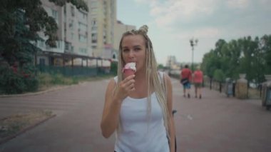 Parkta soğuk pembe dondurma yiyen örülmüş sarışın kadın.