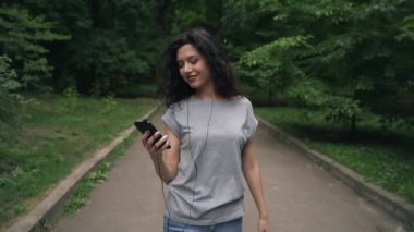 güzel esmer kadın gülümseyen ve parkta oyuncudan müzik dinliyor