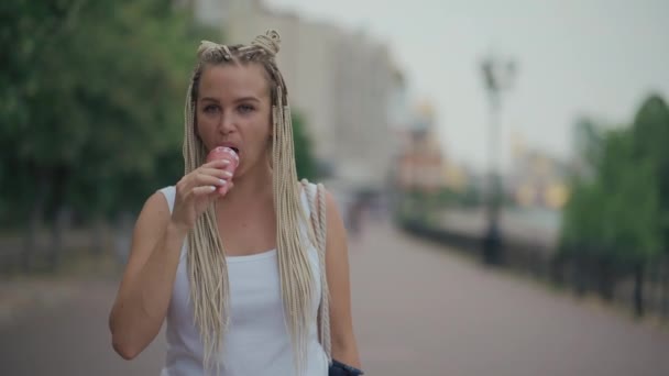 Tressée blonde femelle manger froid rose glace dans le parc — Video