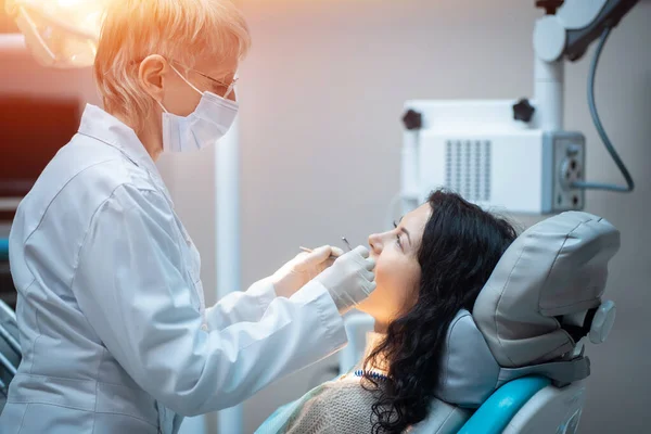 Bela morena encaracolado feminino dentista tratar paciente na clínica moderna — Fotografia de Stock