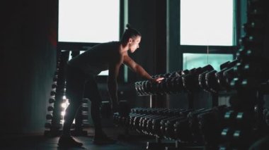 Mükemmel gövdeli atletik adam spor salonunda dambıllarla egzersiz yapıyor.