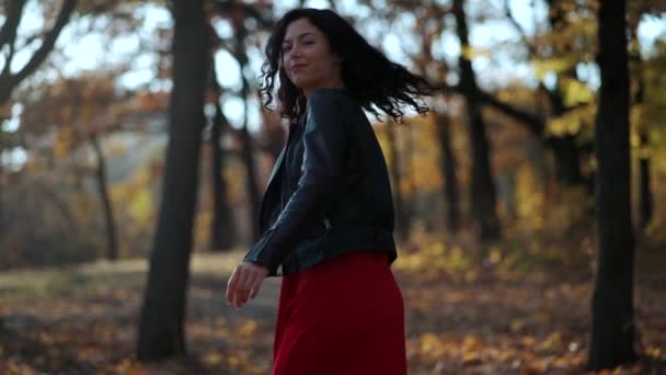 Güzel kıvırcık esmer kadın sonbahar parkında yürüyor ve gülümsüyor. — Stok video