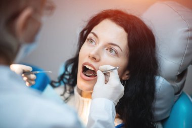 Güzel esmer kıvırcık kadın dişçi modern klinikteki hastayı tedavi ediyor.