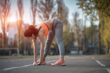 Çekici esmer kadın ısınıyor ve gün ışığında parkta esniyor.