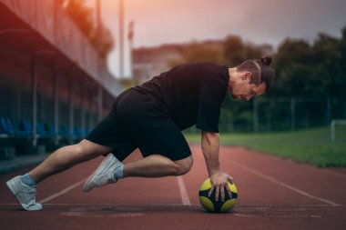 Genç kaslı sporcu antrenman yapıyor ve dışarıda sağlık topuyla egzersiz yapıyor.