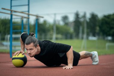 Genç kaslı sporcu antrenman yapıyor ve dışarıda sağlık topuyla egzersiz yapıyor.