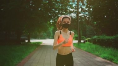 aktif ve genç esmer kadın sabah parkında maskeyle koşuyor.