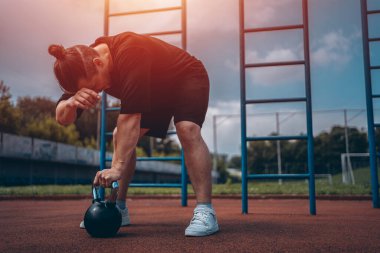  Yorgun bir sporcu dışarıda kettlebell ile spor yapıyor.