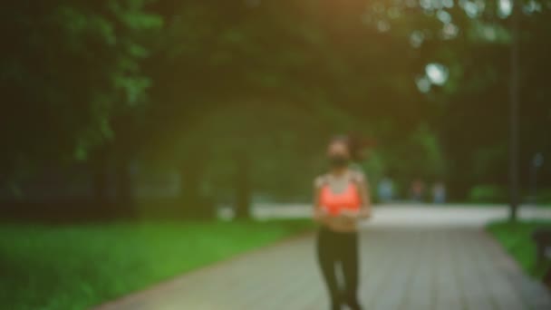 Активная и молодая брюнетка, бегущая в маске на открытом воздухе в утреннем парке — стоковое видео