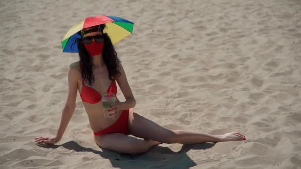 Jong vrouwtje zitten op het strand in medisch masker en drinken kg mojito cocktail — Stockvideo