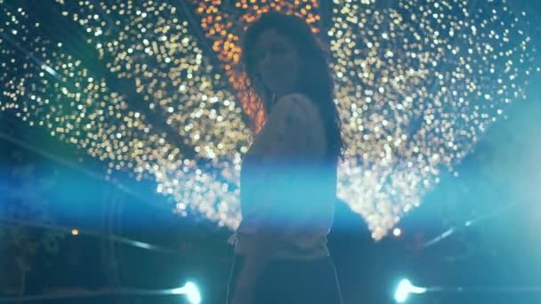 아름답고 곱슬곱슬 한 머리의 브라 운트 여인 이미소를 짓고 도시의 밤에 밝은 야외를 걷고 있다 — 비디오