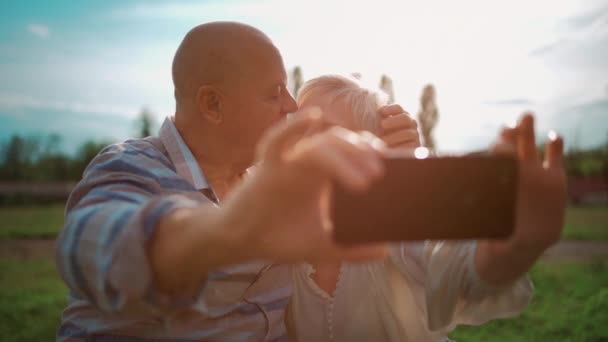 Щаслива старша пара зустрічається і приймає селфі зі смартфоном на свіжому повітрі на заході сонця — стокове відео