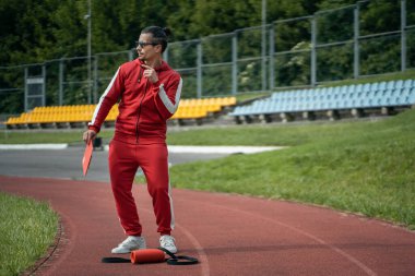 Koşu parkurunda ve tabletle koşan neşeli bir spor eğitmeni.