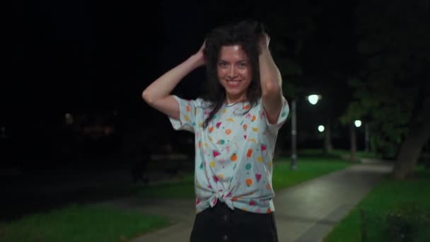 Schattig aantrekkelijk tiener brunette vrouw lopen en dansen in licht nacht park buiten — Stockvideo