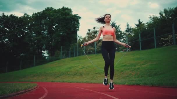Молода атлетична жінка стрибає на пропускаючій мотузці і тренується на стадіоні влітку — стокове відео