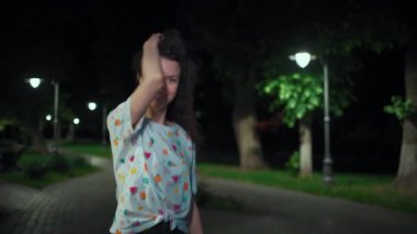 Güzel, çekici, genç, esmer kadın açık hava parkında yürüyüp dans ediyor.