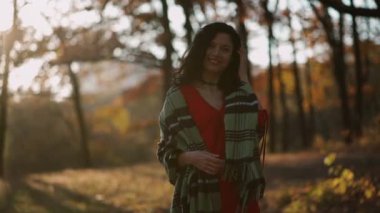 Güzel kıvırcık esmer kadın sonbahar parkında yürüyor ve gülümsüyor.