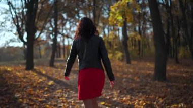 Çekici kıvırcık saçlı kadın güneşli bir günde parkta yürüyor ve gülümsüyor.