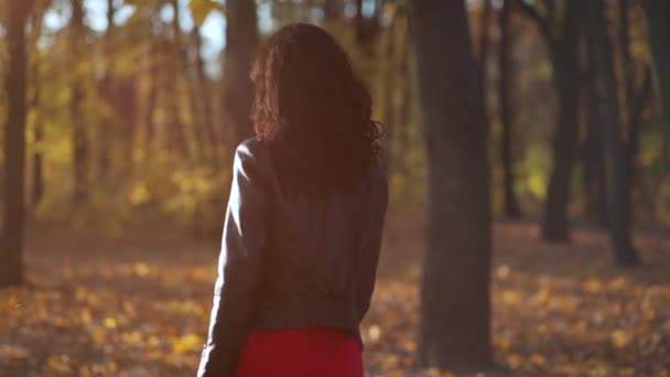 Çekici kıvırcık saçlı kadın güneşli bir günde parkta yürüyor ve gülümsüyor. — Stok video