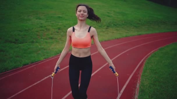 Joven atlética hembra saltando en la cuerda y entrenando en el estadio en verano — Vídeos de Stock