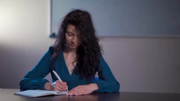 Encaracolado morena mulher fazendo notas na sala de aula da escola — Vídeo de Stock