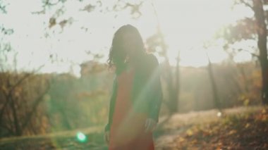 Güzel kıvırcık esmer kadın sonbahar parkında yürüyor ve gülümsüyor.